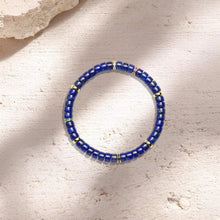 Blue beaded bracelet with gold and colored accent beads on textured beige surface