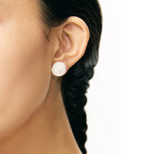 Close-up of a woman's ear wearing modern white spiral stud earrings with braided dark hair