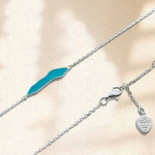 Delicate silver chain necklace with turquoise abstract pendant and Buddha charm on textured beige surface