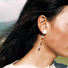 Close-up of woman wearing long dangling earrings with white rose design and colorful beads