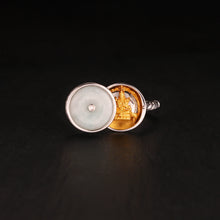 Silver locket ring opened revealing golden Buddha statue inside, with a translucent circular cover featuring a small gem