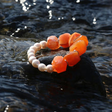 Orange raw stone and white bead bracelet on wet rock with flowing water background
