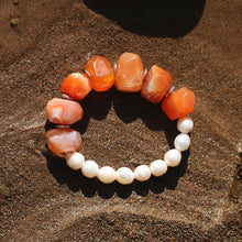 Bracelet with orange agate and white round pearls on wet sandy beach