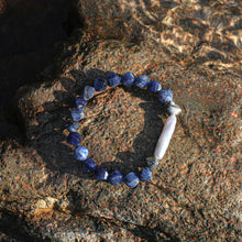 Blue sodalite bead bracelet with a white baroque pearl on textured rock surface in sunlight