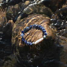 Blue sodalite bead bracelet with a white pearl centerpiece resting on wet rock under flowing water