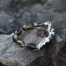 Handmade bracelet with polished dark agate and spotted white jasper beads on a textured rock