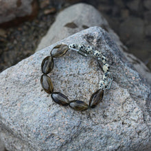 Chunky bracelet with smoky quartz and spotted bead charms on rough stone surface
