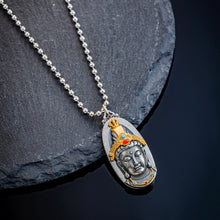 silver pendant necklace with a detailed Buddha face and colorful crown on black stone background