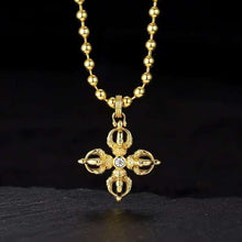 Gold pendant necklace with ornate cross design and central clear gemstone on gold bead chain