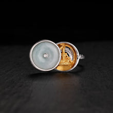 Silver ring with jade disc lid and gold Manjushri Bodhisattva statue inside on black surface