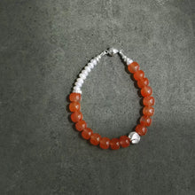 Beaded bracelet with translucent orange and white pearls on gray background