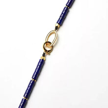 Close-up of blue cylindrical bead necklace with gold oval clasp on white background
