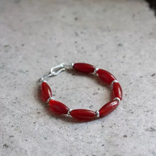 Red beaded bracelet with silver spacers on a textured stone surface