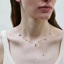 Close-up of woman wearing silver charm necklace with red and black teardrop pendants and white top