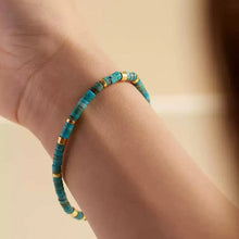 Close-up of wrist wearing a turquoise and gold beaded bracelet on neutral background