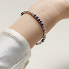silver and blue beaded bracelet on wrist in white sleeve against light background