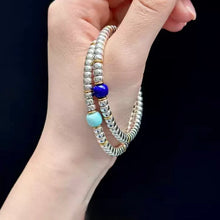 Hand holding two silver beaded bracelets with blue and turquoise beads on black background