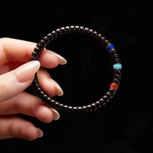 Hand holding a black beaded bracelet with blue, turquoise, and red accent beads on black background