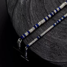 Close-up of two beaded bracelets with silver and blue beads on textured black surface