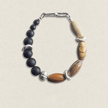 Handmade bracelet with matte black round beads, polished brown stone beads, and silver metal accents on light background