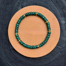 Green malachite bead bracelet with gold accents on tan leather circle background