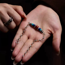 Hand holding silver chain bracelet with red, blue, and turquoise beads and a silver ring on finger