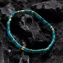 Turquoise and gold beaded bracelet on textured dark volcanic rock surface