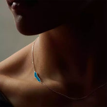 Close-up of a person wearing a delicate silver necklace with a small blue pendant on the neck