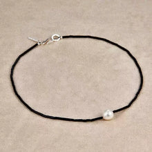 Minimalist black beaded necklace with single white pearl centerpiece on beige background