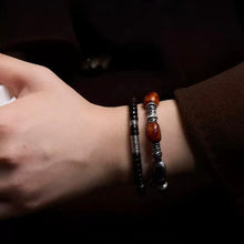 Close-up of wrist wearing black and brown beaded bracelets with silver accents on dark background