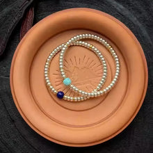 Silver beaded bracelets with blue and turquoise beads on terracotta plate over black fabric