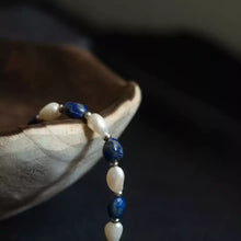 Pearl and blue gemstone beaded bracelet draped over wooden bowl against dark background