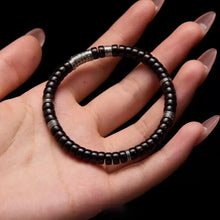 Hand holding black beaded bracelet with silver accents on black background