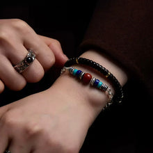 Close-up of a wrist wearing two beaded bracelets and a silver ring with black stone on the finger