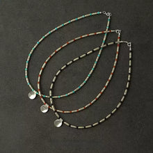 Three beaded necklaces with cylindrical silver and colored turquoise, red, and black beads, each with a round silver pendant on black background