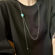 Person wearing a black round-neck top and a silver lariat necklace with a turquoise stone pendant