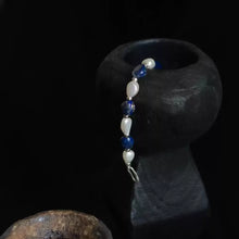 Blue and white beaded bracelet draped over textured black and brown pottery against black background