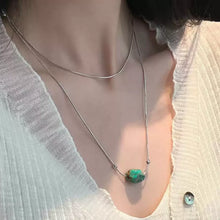 Close-up of a person wearing layered silver necklaces with a turquoise stone pendant and a beige knitted top