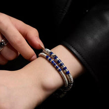 Close-up of hand wearing silver and blue beaded bracelets on wrist with black leather sleeve background
