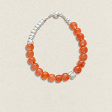 Elegant bracelet with orange translucent beads, white pearls, and silver clasp on beige background