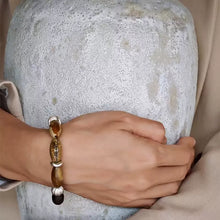 Close-up of hand wearing brown and silver beaded bracelet resting on textured gray stone