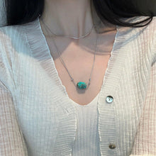 Close-up of person wearing a silver chain necklace with turquoise stone pendant and white ribbed cardigan