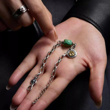 Hand holding silver chain bracelet with green stone bead and round charm featuring Greek letter