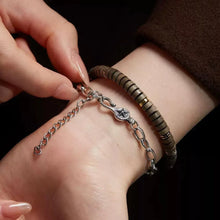 close-up of wrist wearing a silver star charm bracelet and a brown beaded bracelet with gold accents
