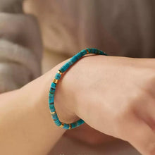 Turquoise and gold bead bracelet on a wrist with a blurred neutral background