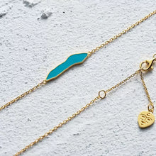 Gold chain bracelet with turquoise enamel irregular-shaped centerpiece on textured white surface