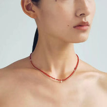 Close-up of a woman wearing a layered red beaded and gold chain necklace on bare shoulders