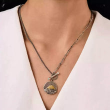 Person wearing two silver necklaces with a round pendant featuring a mountain design