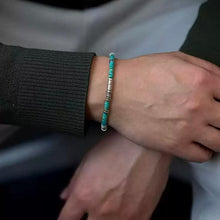 Close-up of a wrist wearing a turquoise and silver beaded bracelet with a black ribbed sleeve