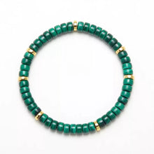 Green and gold beaded bracelet with polished roundstones on white background